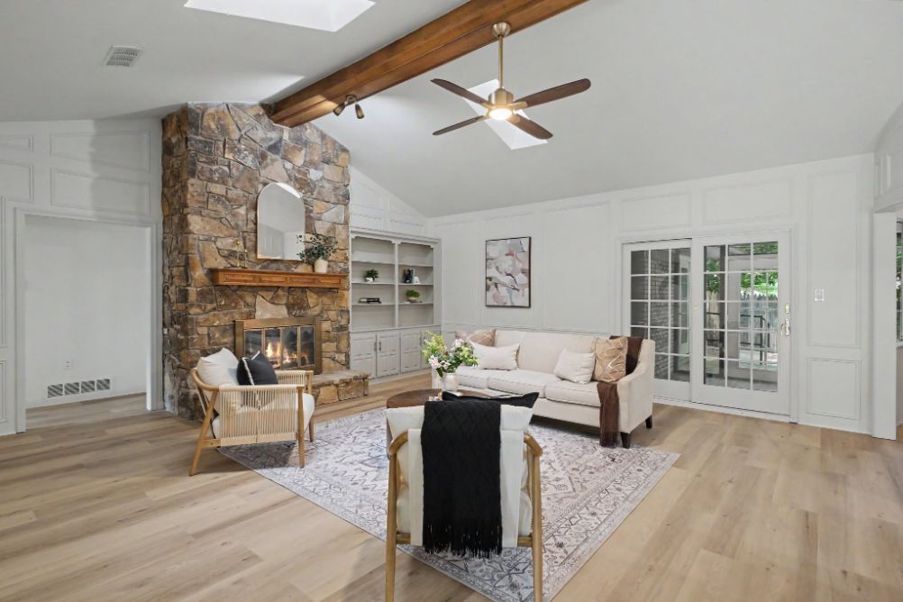 Wide view of the staged living room with stone fireplace and architectural beams